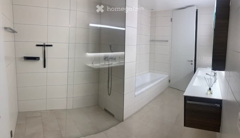 Modern bathroom with white tiles, a bathtub, a sink, a large mirror, and a glass-enclosed shower area.