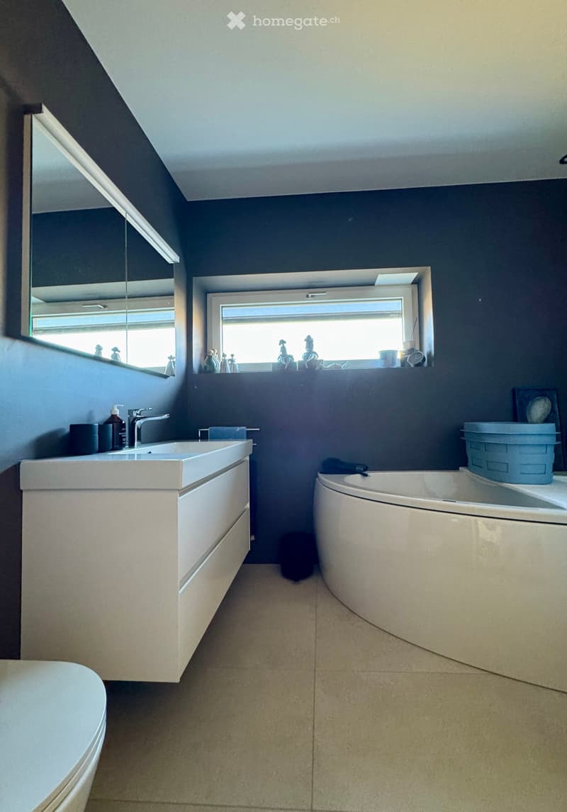 Modern bathroom with white fixtures, bathtub, large mirror, window, storage cabinet, ceramic floor