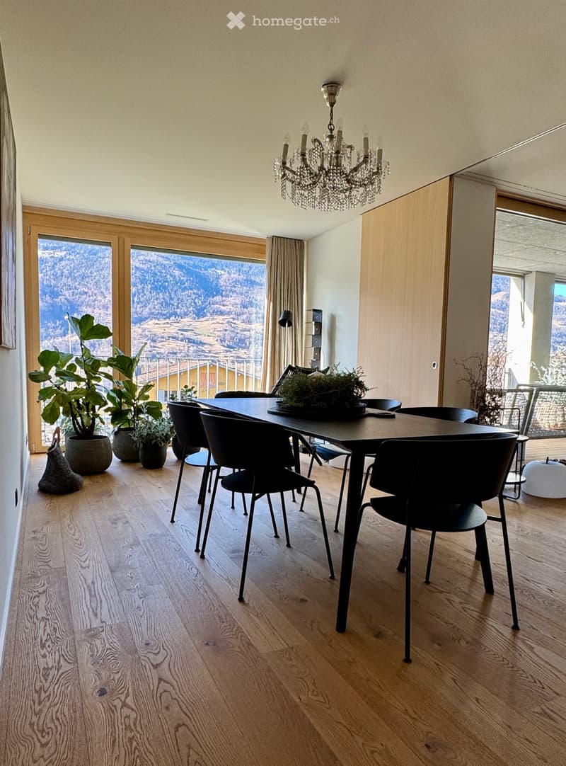 dining table, black chairs, chandelier, large glass windows, wooden floor, plants, balcony with railing