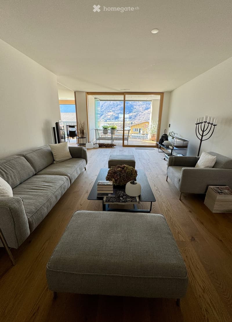 wide living room, wooden floor, gray couches, sliding doors, wooden balcony with views of the mountains, coffee table, white lights, glass wall