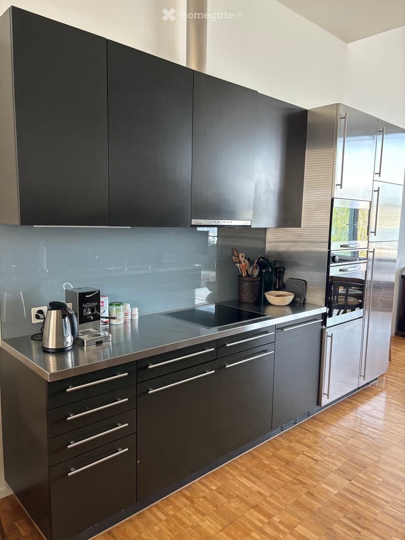 Modern kitchen with dark grey cabinets, stainless steel appliances, and a sleek countertop. Features include an induction stove, refrigerator, electric kettle, toaster, and various kitchen utensils.