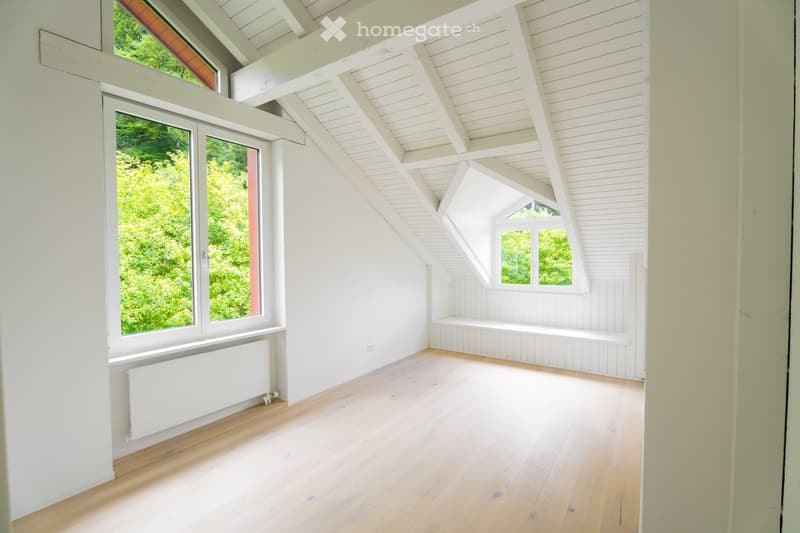 Bright, empty room with wooden flooring, white walls, large windows, and a slanted white ceiling. No furniture or equipment present.