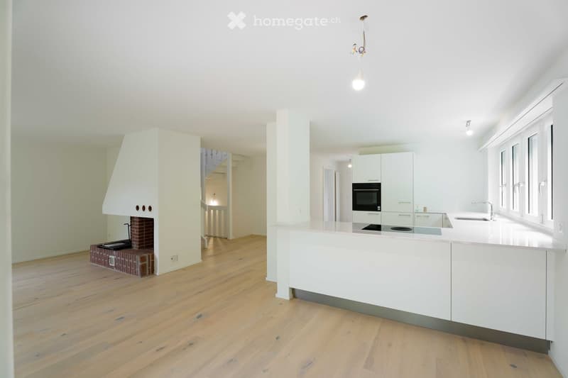 Bright, modern kitchen with white cabinetry, a central island, and a built-in fireplace. The space features light wooden flooring and ample natural light from large windows.