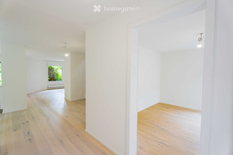Empty room with light wooden flooring and white walls, featuring a window with a view of greenery and a radiator below it.