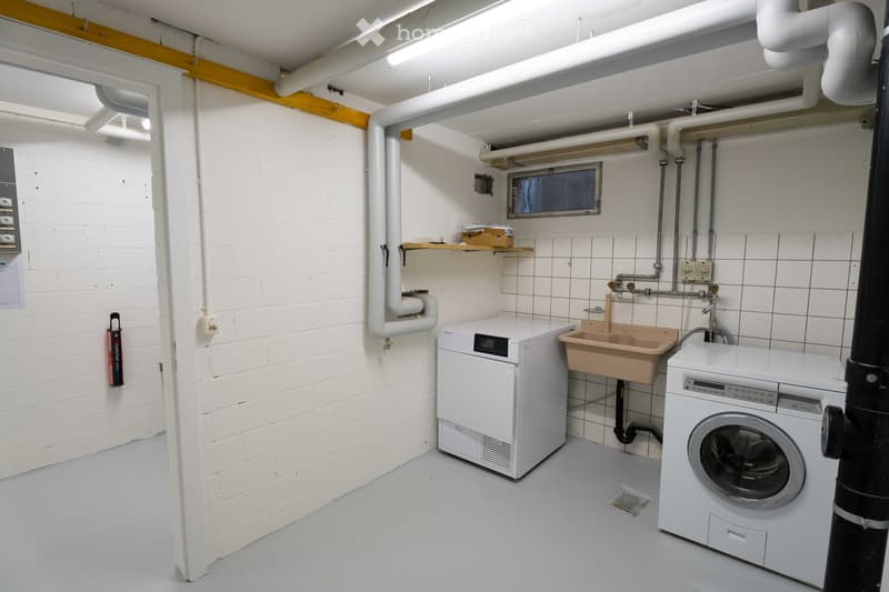 Utility room with white brick walls, tiled floor, washing machine, dishwasher, and sink.