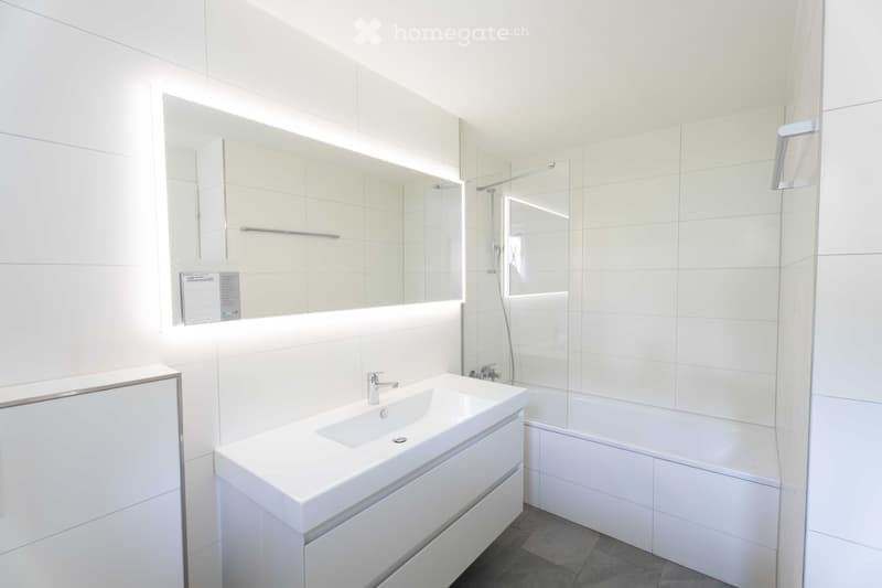 Modern bathroom with white tiles, a sink with a modern faucet, a bathtub, and a large mirror with built-in lighting.