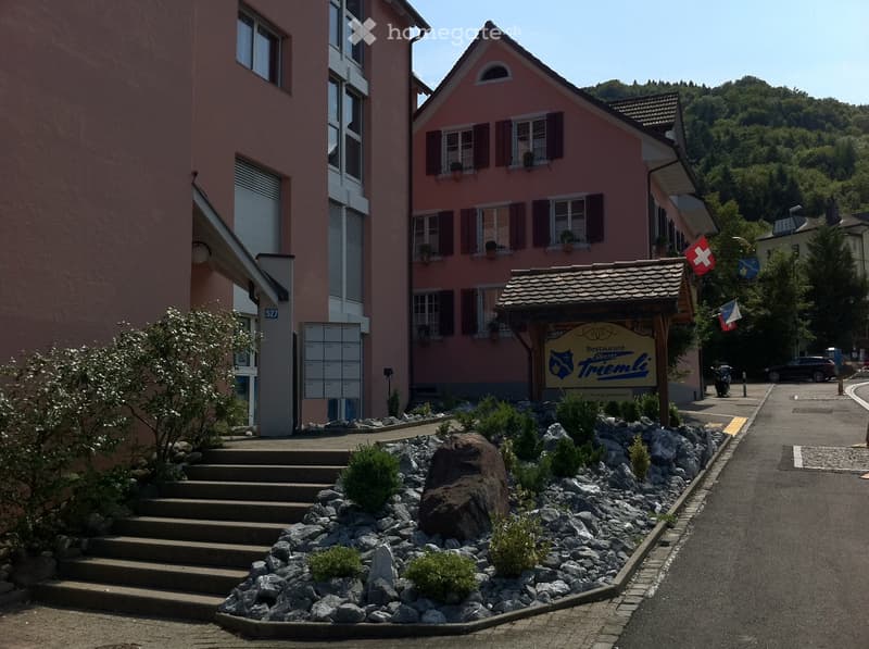 Buildings with staircases, flags, a road, greenery, and a sign