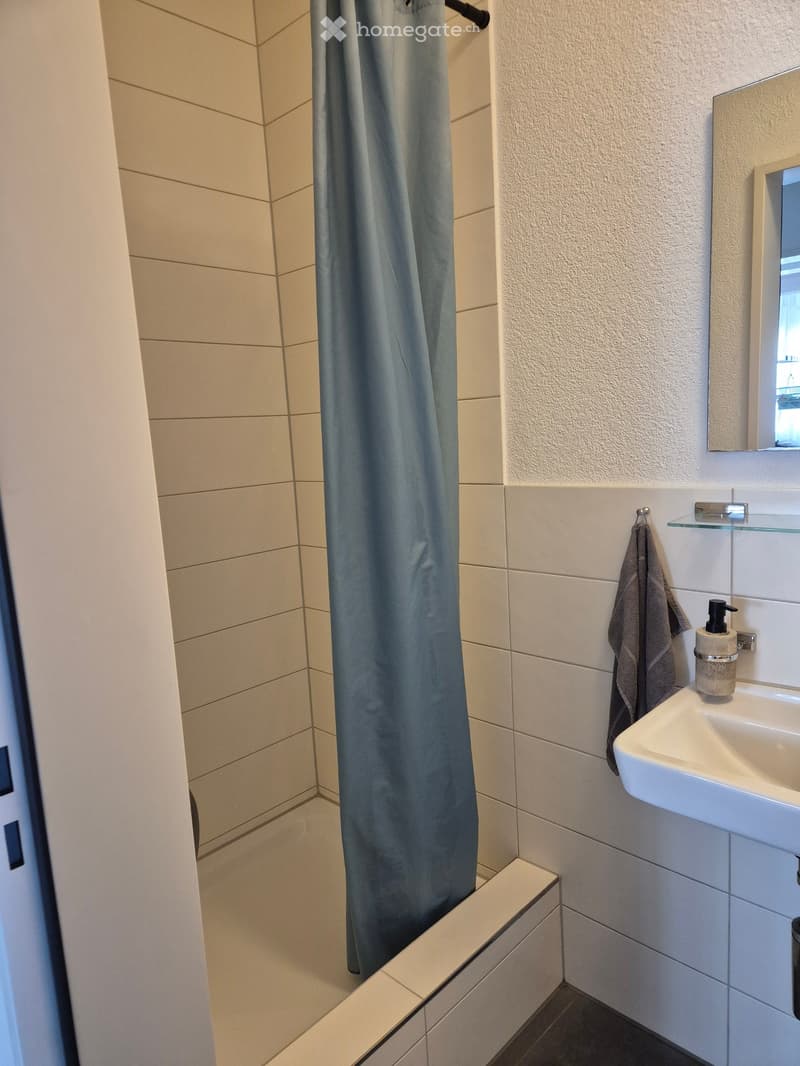 Modern bathroom with a white sink, mirror, towel, and a shower with a blue curtain.