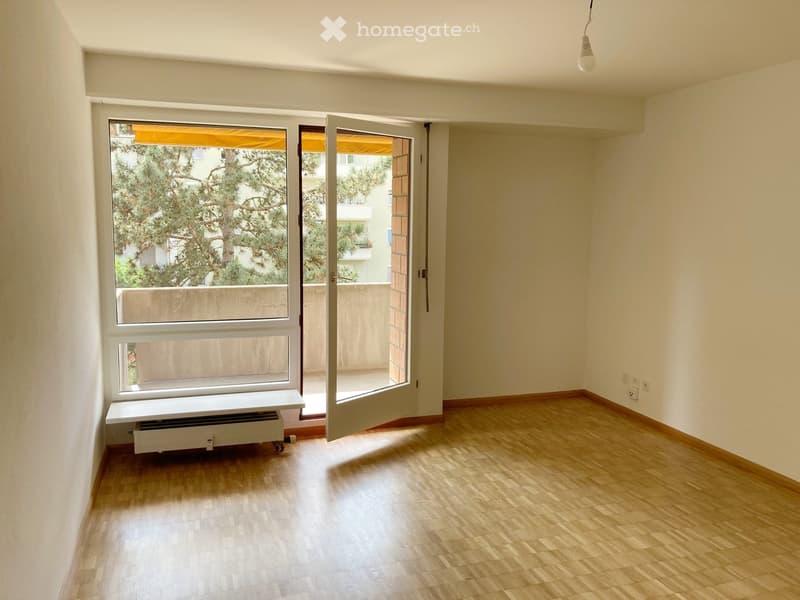 Empty room with wooden flooring, large windows, and an open door leading to a balcony.