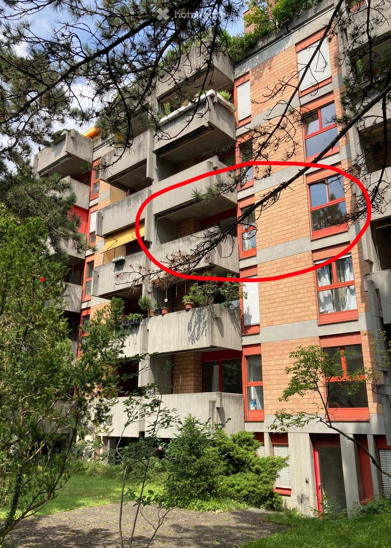 Multi-story residential building with concrete and brick facade, balconies, and greenery.