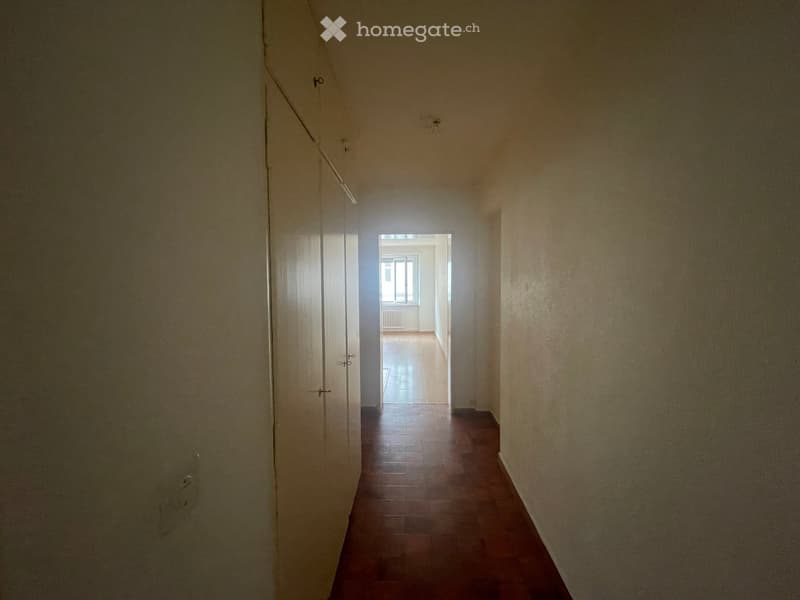 Empty hallway with wooden flooring, white walls, and a door leading to another room.