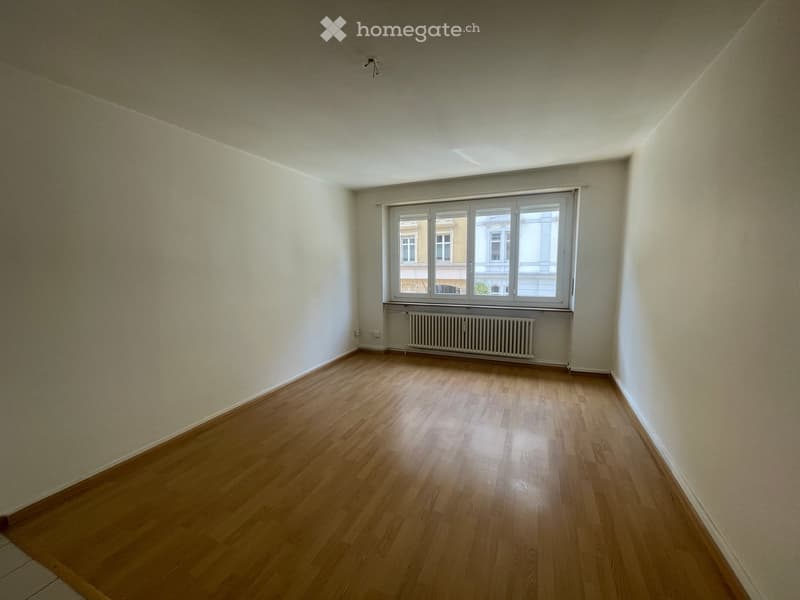 Empty room with wooden flooring, white walls, and a large window with a radiator below it.