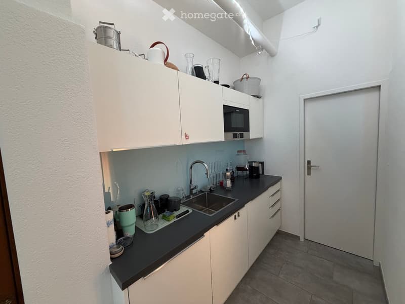 Modern kitchen with white cabinets, black countertop, stainless steel sink, microwave, and various appliances.