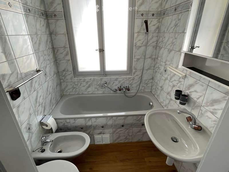 Bathroom with marble tiles, bathtub, sink, bidet, toilet, and a mirror above the sink.