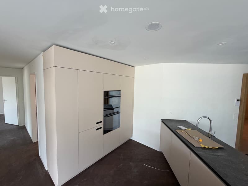 Empty kitchen with light-colored cabinets, a black countertop, and a sink with a modern faucet. The floor is dark wood, and the walls are white.