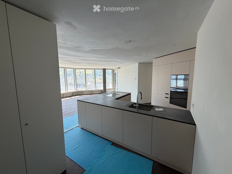 Modern kitchen with white cabinets, black countertop, stainless steel sink, and built-in oven. Large windows provide natural light.