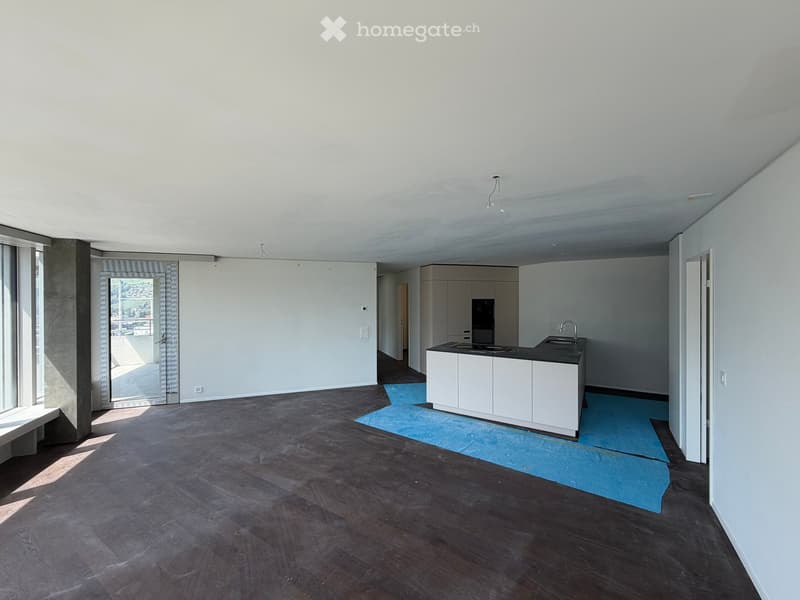 Empty room with wooden flooring, white walls, and a small kitchen area with cabinets and a sink.