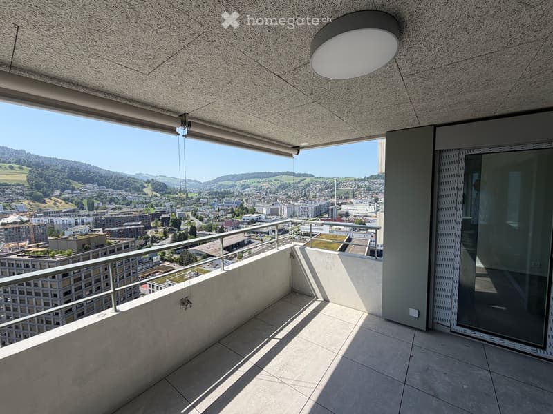 Modern balcony with concrete floor, metal railing, large window offering panoramic city and landscape view.