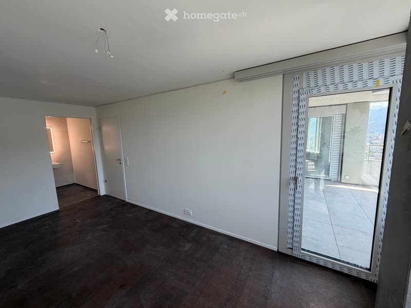 Empty room with wooden flooring, white walls, and a large glass door leading to a balcony. There is a visible doorway to another room on the left side.