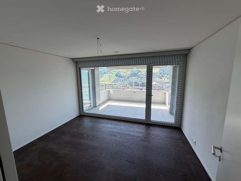 Empty room with wooden flooring, white walls, and large sliding glass doors leading to a balcony with a scenic view.