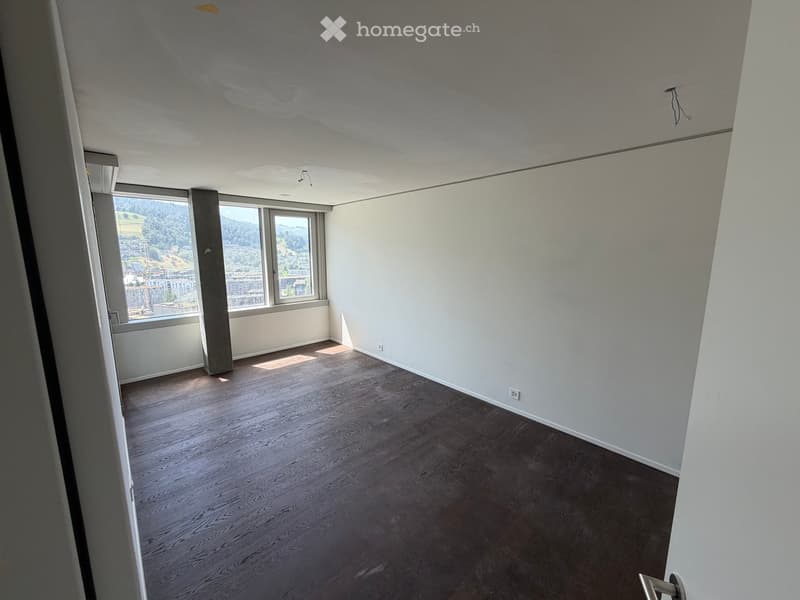 Empty room with wooden flooring, white walls, and large windows offering a scenic view.