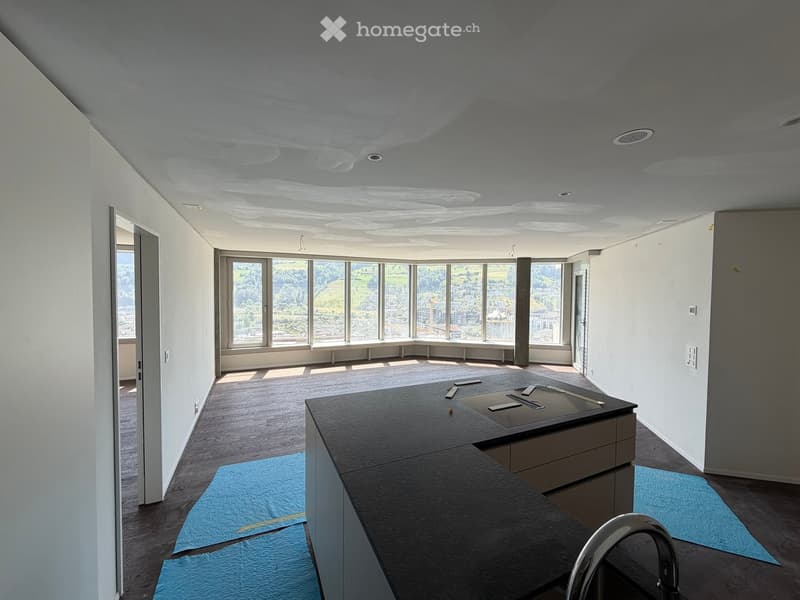 Empty room with wooden flooring, large windows offering a scenic view, and a countertop with tools and materials, indicating ongoing construction or renovation.