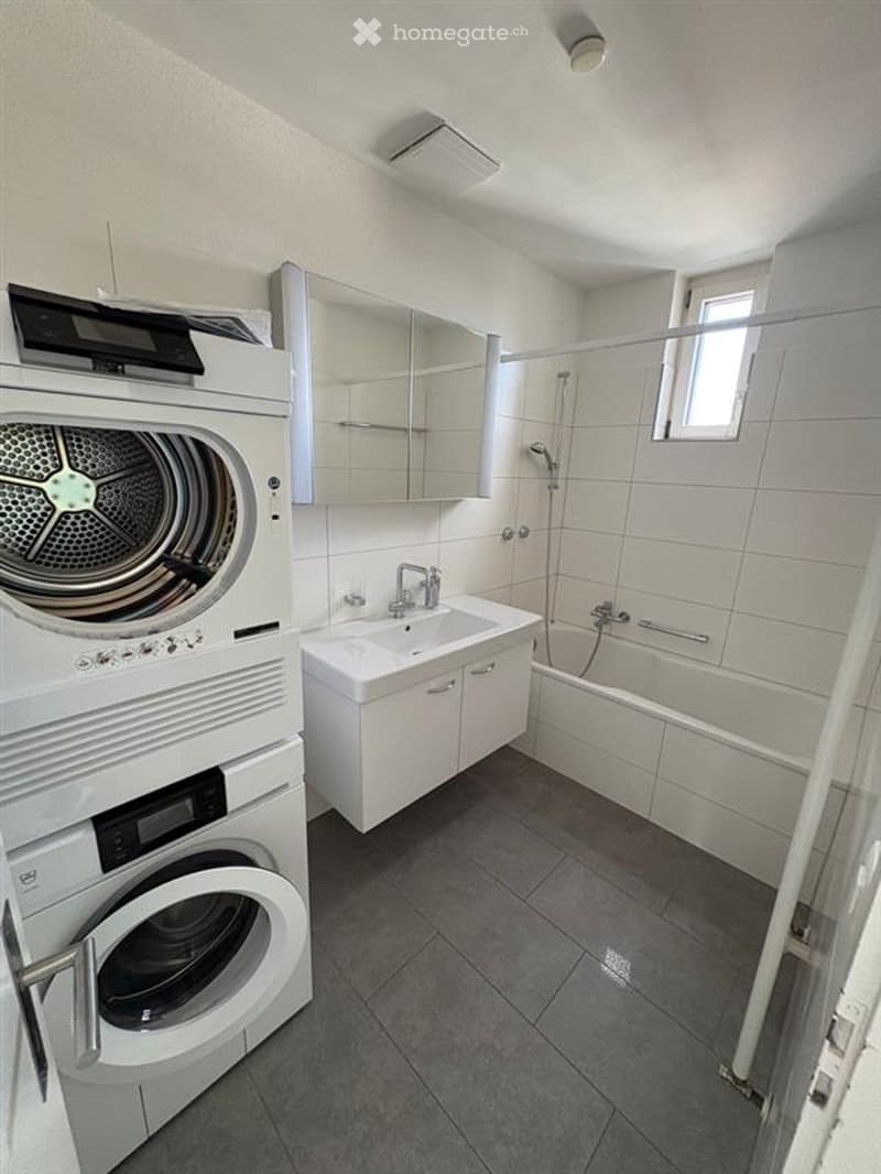 Modern bathroom with white tiles, a sink, bathtub, mirror, and a private washing machine.