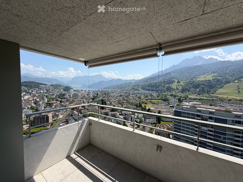 Modern balcony with concrete floor, metal railing, and panoramic view of city and mountains.