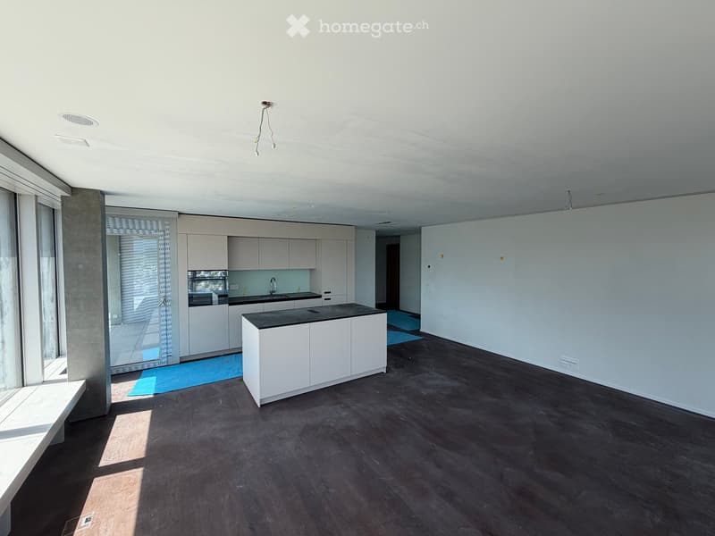 Modern, unfurnished kitchen with white cabinets, dark countertops, and a central island. The space features large windows and a sleek, minimalist design with dark wooden flooring.