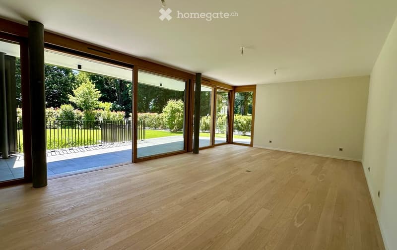 Empty room with wooden flooring, large sliding glass doors leading to a garden, and white walls.