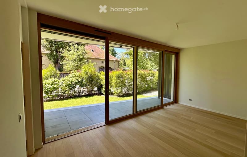 Empty room with wooden flooring, large sliding glass doors leading to a tiled patio and garden area.