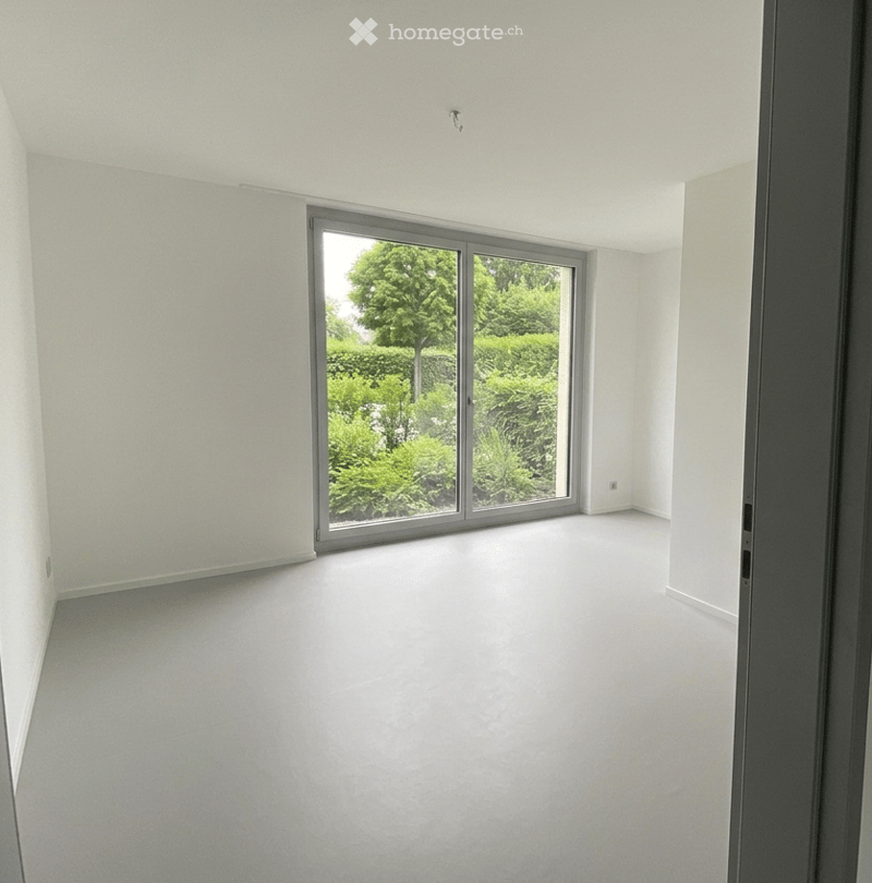 Unfurnished Room. Empty room with white walls, grey carpeted floor, and large sliding glass door leading to a green outdoor area.