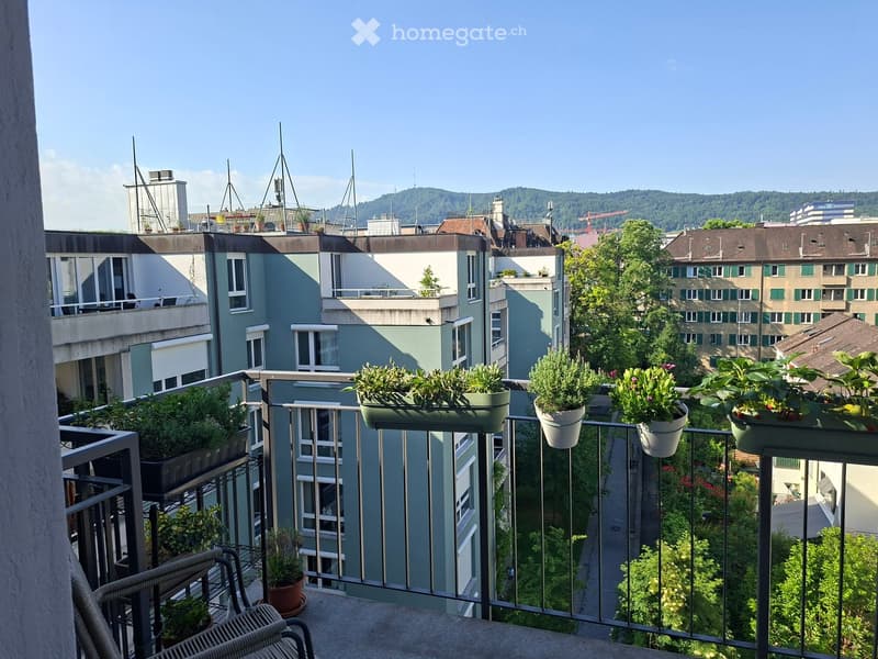 Balcony with metal railing, potted plants, and a view of the cityscape and surrounding greenery.
