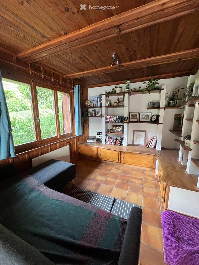 Cozy living room with wooden ceiling, tiled floor, large windows, bookshelf, sofa, and decorative items.