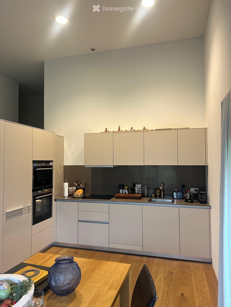 Modern kitchen with light-colored cabinets, stainless steel appliances, and a wooden dining table with a vase and bowl on it.