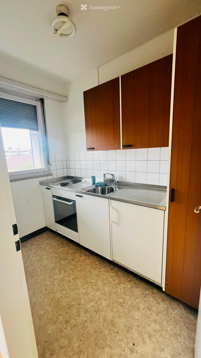 Empty kitchen with white cabinets, a sink, an oven, and a window with blinds.