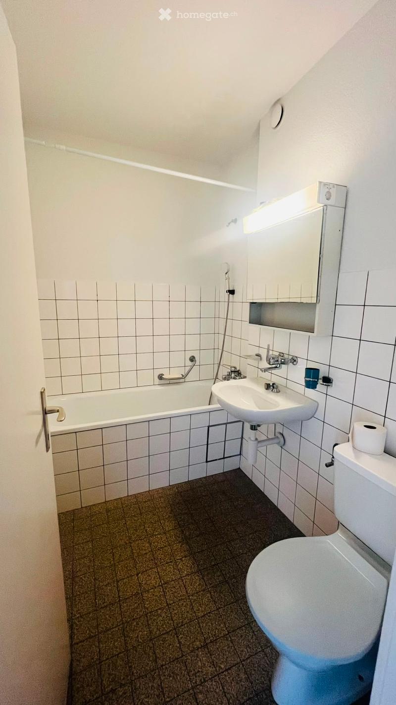Bathroom with white tiled walls, a bathtub, a sink, a toilet, a mirror, and a cup on the sink.