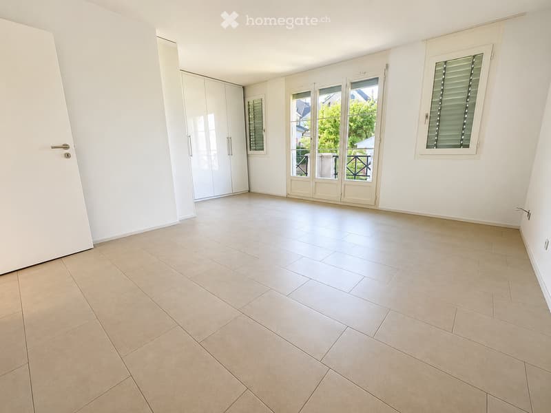 Empty room with tiled floor, white walls, large sliding glass doors leading to a balcony, and built-in closet with mirrored doors.