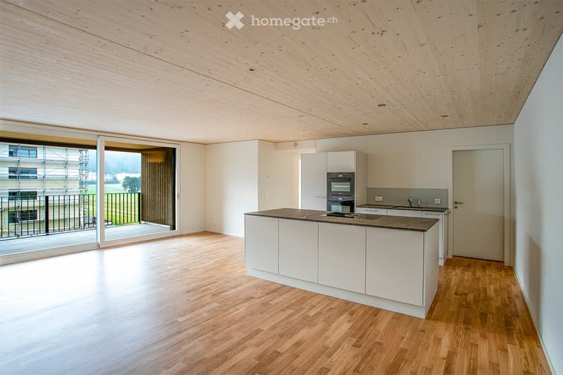 Modern kitchen with white cabinets, a central island, and a sleek oven. The space features light wooden flooring and large windows with a view of the outdoors.