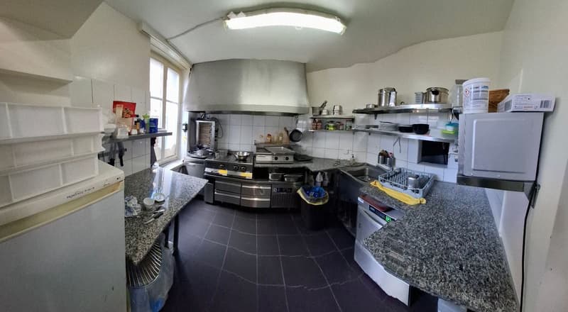 Commercial kitchen with stainless steel appliances, granite countertops, and shelves stocked with kitchenware and supplies.