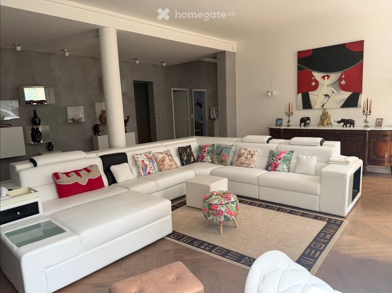 Modern living room with white sectional sofa, colorful throw pillows, glass coffee table, patterned rug, and decorative items including vases and a painting.