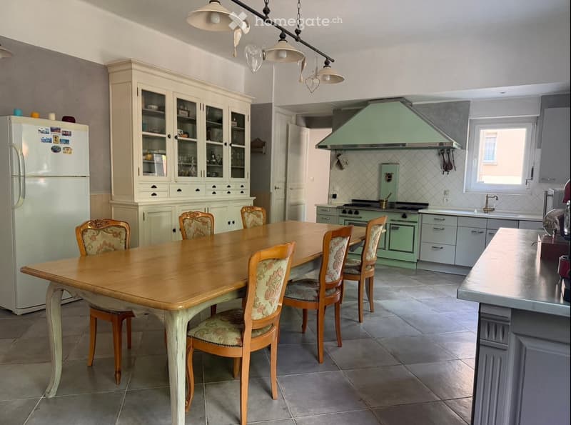A well-furnished kitchen with a wooden dining table, six chairs, a refrigerator, cabinets, a stove, and a sink.