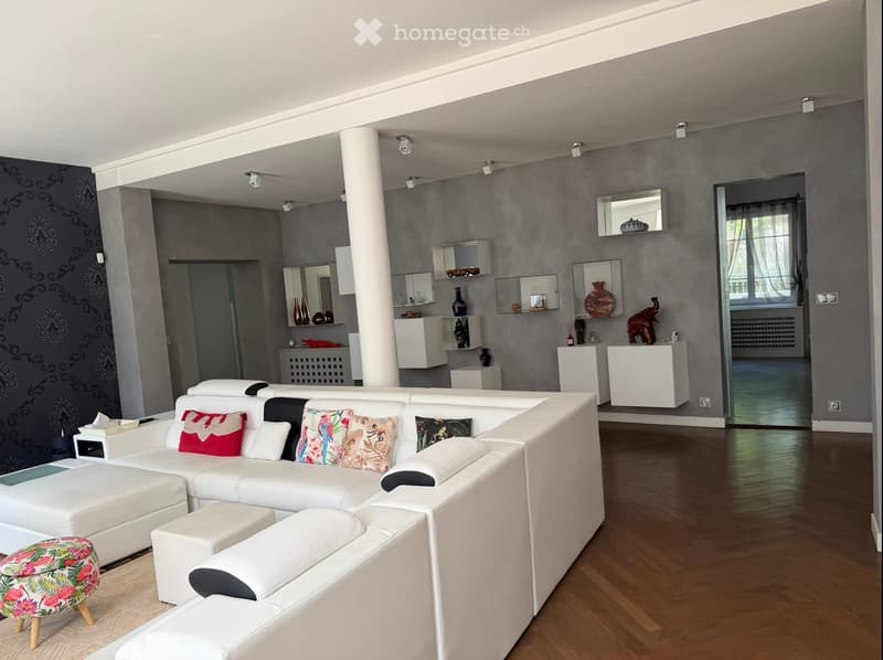 Modern living room with white sectional sofa, colorful cushions, a floral stool, and decorative shelves with vases and artwork.