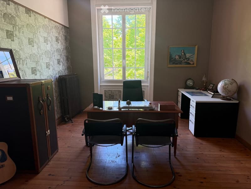 A well-furnished room with wooden flooring, a large window, a desk with chairs, a globe, a cabinet, and a guitar leaning against the wall.