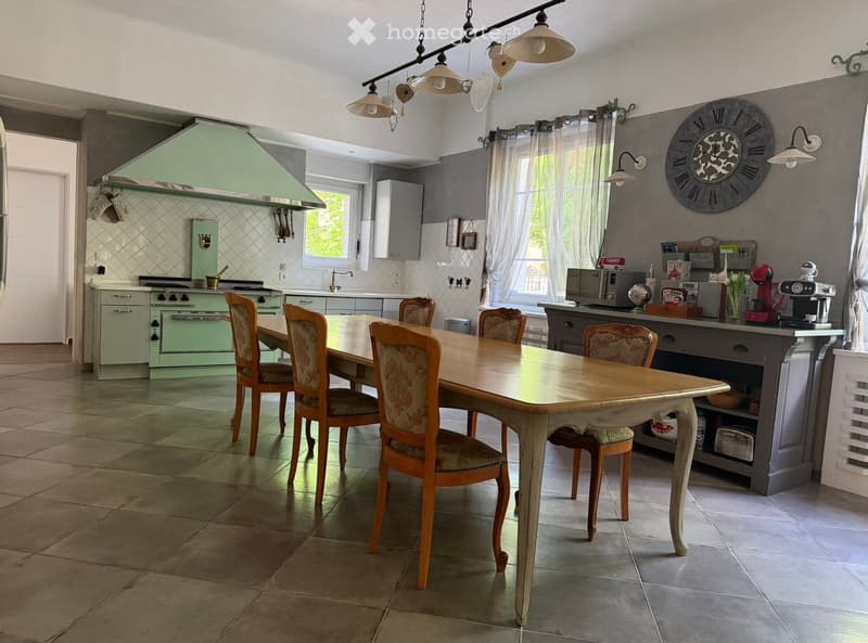 Bright kitchen with a dining area, featuring a wooden dining table with six chairs, a green oven, microwave, coffee maker, and various kitchen cabinets and appliances.