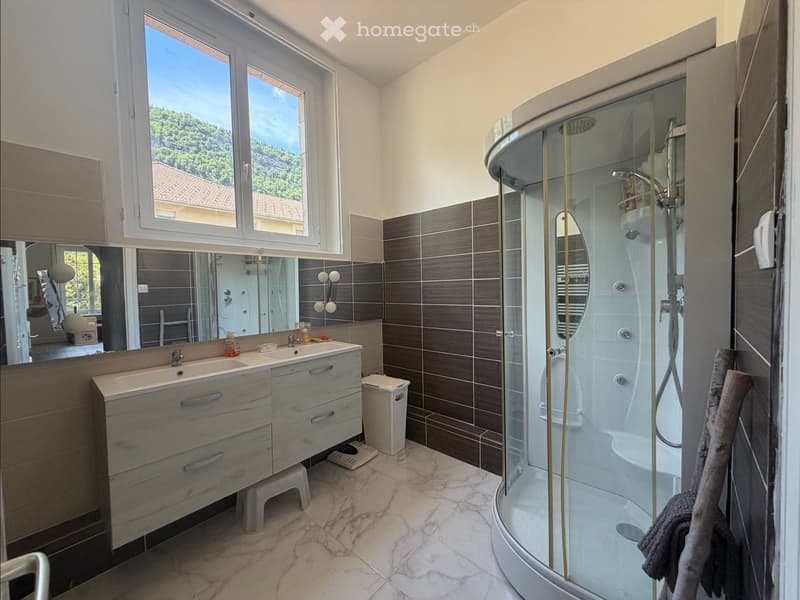 Modern bathroom with a double sink vanity, large mirror, glass-enclosed shower, marble flooring, and a view of greenery outside the window.
