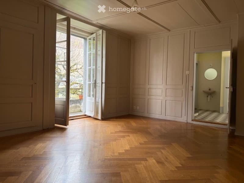 Empty room with wooden flooring, large open doors leading to a balcony, and a small adjacent bathroom visible.