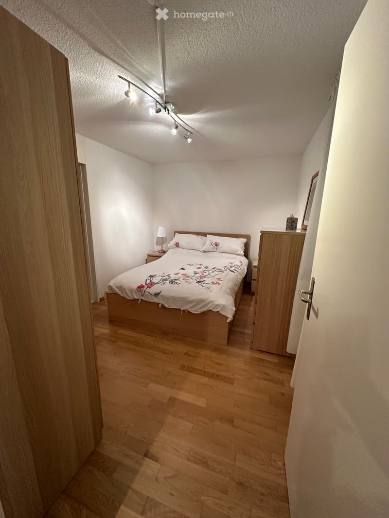 Cozy bedroom with wooden flooring, a double bed with floral bedding, a nightstand with a lamp, and a wooden wardrobe.