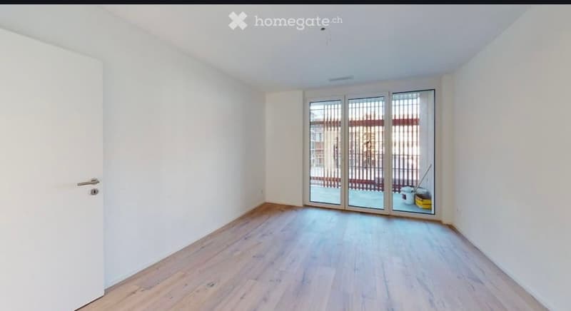 Empty room with light wooden flooring, white walls, and large sliding glass doors leading to an outdoor area.