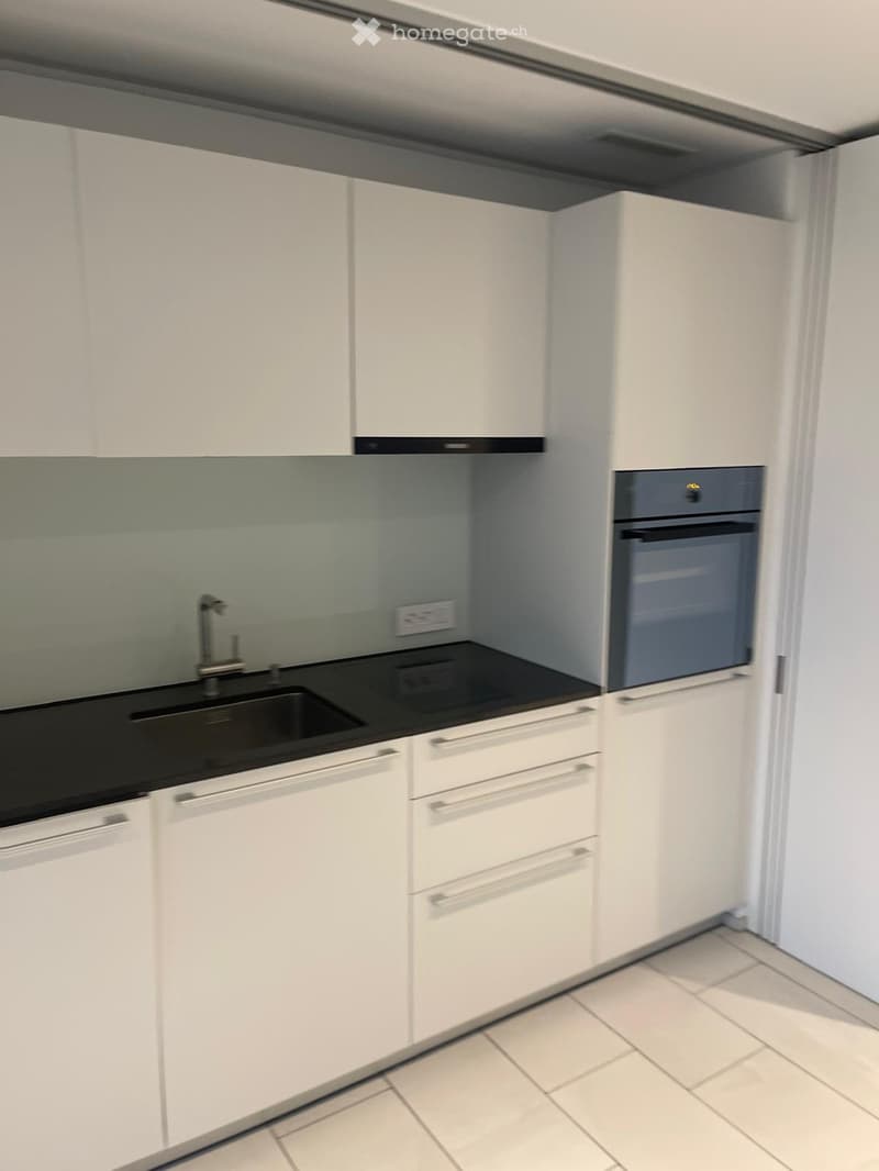 Modern kitchen with white cabinets, black countertop, sink, faucet, and built-in oven.